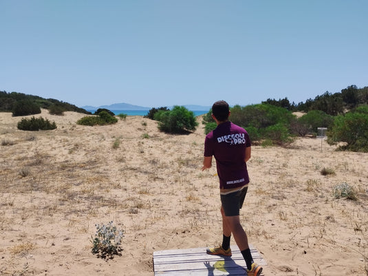 Tee Pad auf einer der DiscGolf Bahnen des ersten DiscGolf Parcours in Griechenland mit DiscGolfer beim Abwurf an der Strandbahn