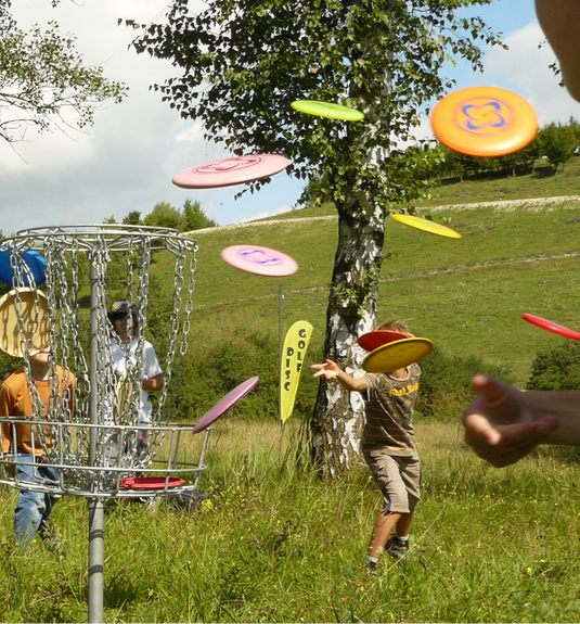 Viele bunte DiscGolf Scheiben die von Kindern in einen Korb geworfen werden.